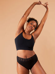 Woman stretching with a relaxed expression, wearing black lacy period pants.