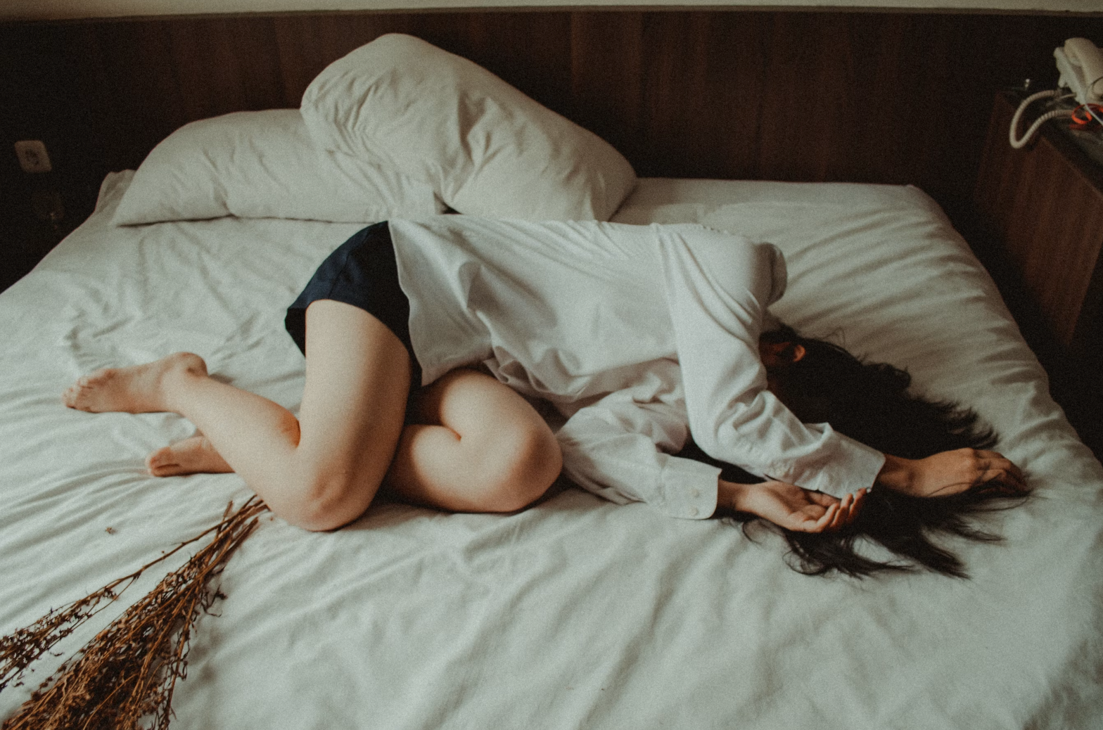 A woman lying curled up on a bed, holding her stomach, representing discomfort from IBS and period pain.