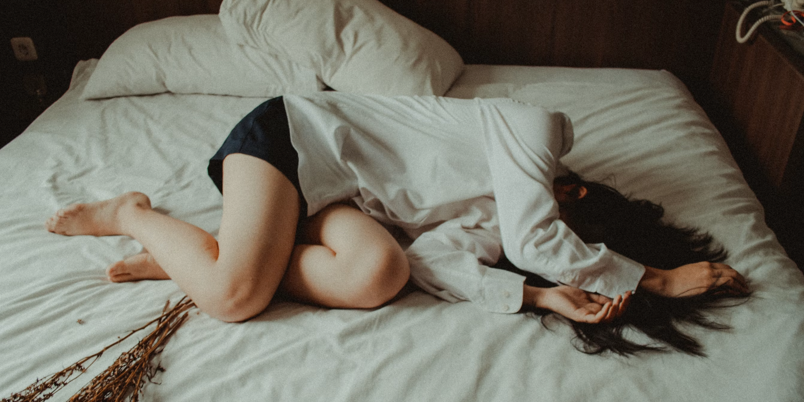 A woman lying curled up on a bed, holding her stomach, representing discomfort from IBS and period pain.