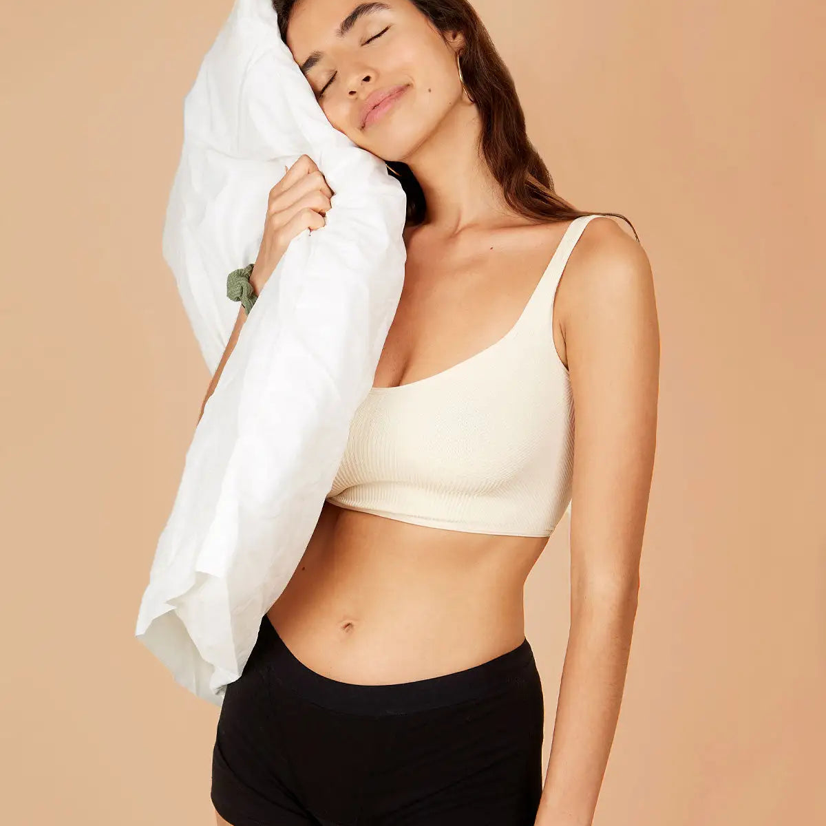 Woman wearing boxer-style sleep shorts, holding a pillow to her head, looking relaxed.